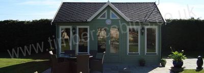 Green painted log cabin summer house with shingle roof on a patio